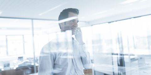 junger dunkelhaariger Mitarbeiter telefoniert hinter einer Glasscheibe 